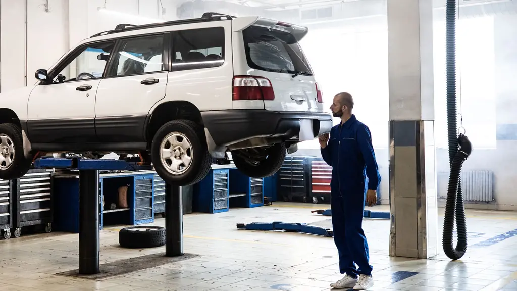 A mechanic next to a car raised on a lift in a bright workshop